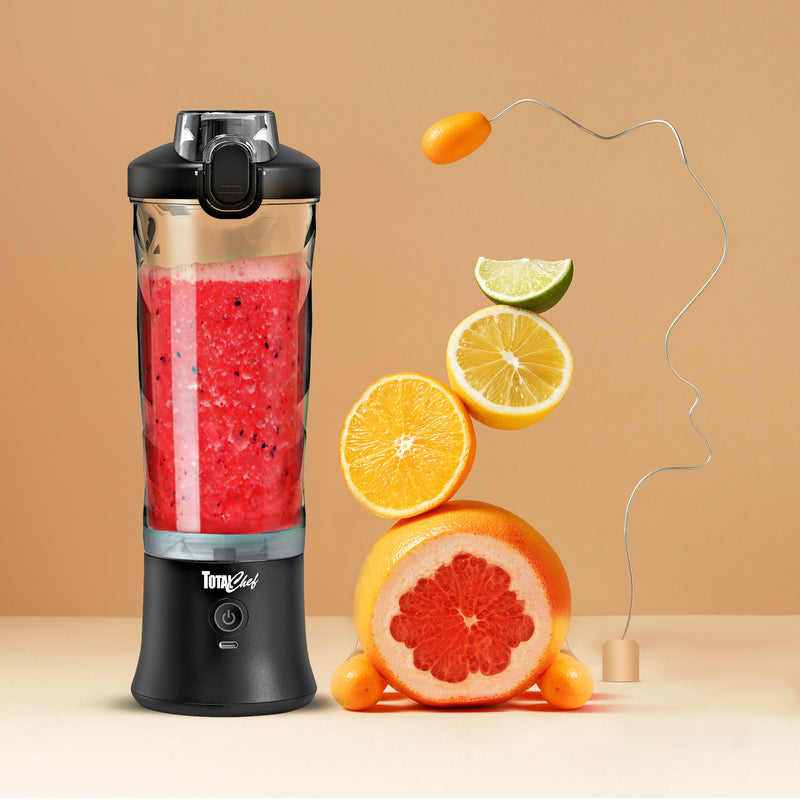 Lifestyle image of the Total Chef USB chargeable blender filled with bright red smoothie on a light orange-yellow background with a stack of sliced citrus fruit beside it.