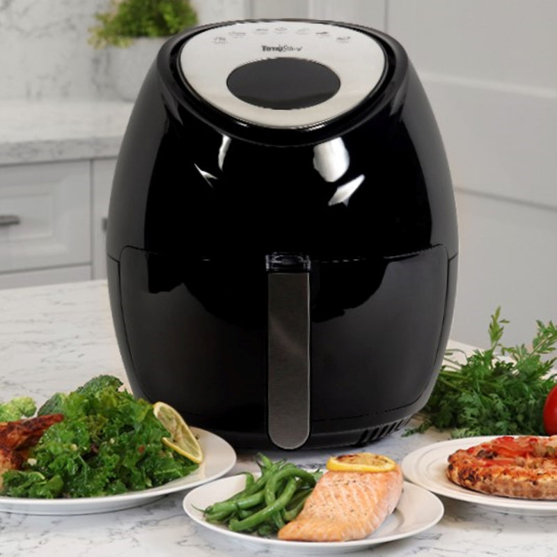 Lifestyle image of Total Chef air fryer on a white marble counter surrounded by plates of cooked food plus uncooked tomatoes and herbs