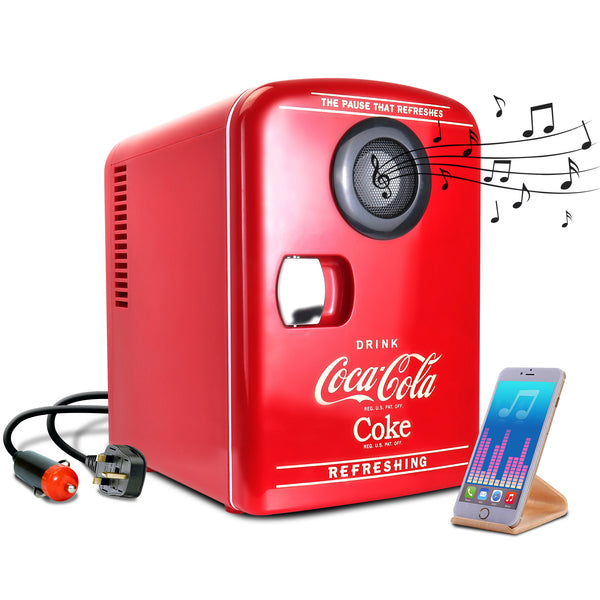 Product shot of Coca-Cola 4L mini fridge with Bluetooth speaker, closed, with AC and DC power cords visible, on a white background. There is a smartphone or music player on a stand in the foreground and small black music notes emanating from the speaker 